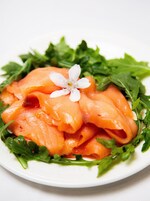 Un plato de salmón ahumado con una decoración floral sobre una cama de hojas verdes.