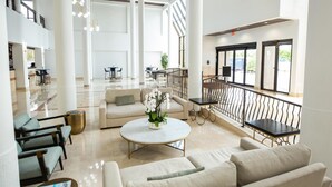 A spacious lobby with high ceilings, large windows, and a central seating area with a round table and sofas.