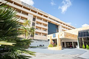 A hotel with a modern design, featuring a large entrance and a parking area.