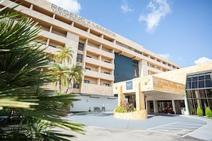 A hotel with a modern design, featuring a large entrance and a parking area.
