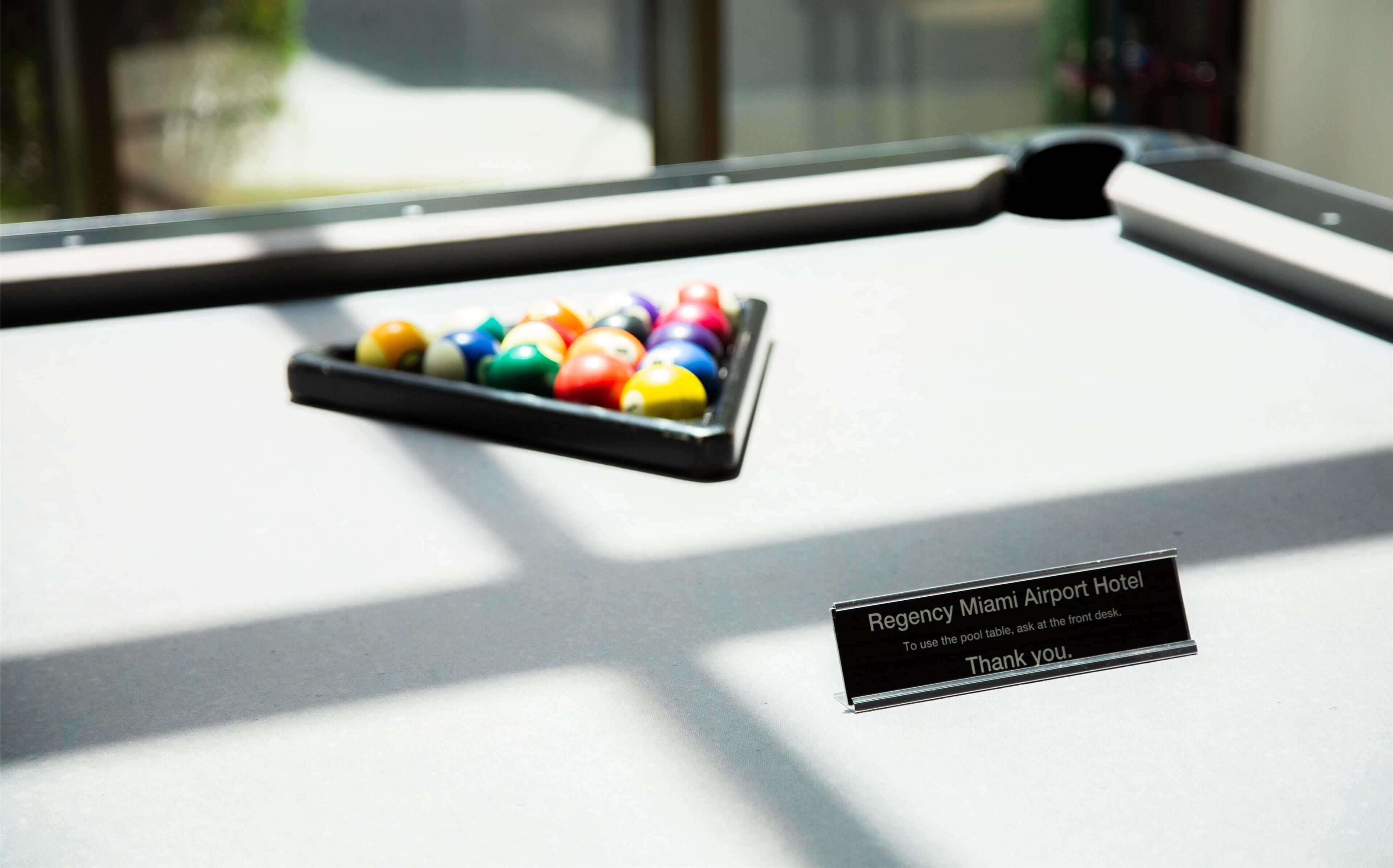 Uma mesa de bilhar com bolas coloridas e uma placa indicando que o local é o Regency Miami Airport Hotel.