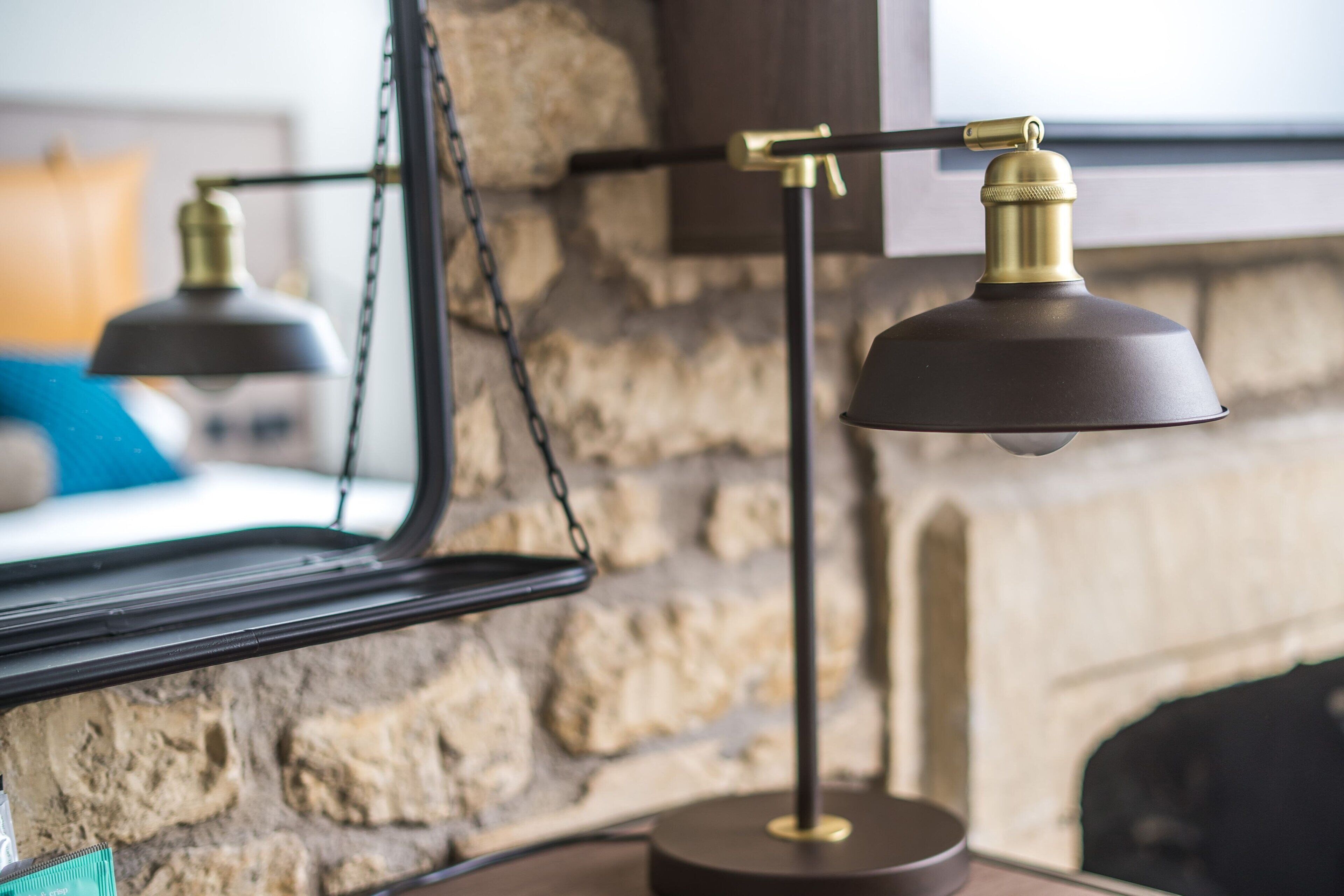 Une lampe moderne avec un abat-jour noir et des détails en laiton, fixée à un mur dont la texture rappelle celle de la pierre.