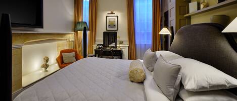 A hotel room with a large bed, a flat-screen TV mounted on the wall, a desk with a chair, and a bookshelf with decorative items.