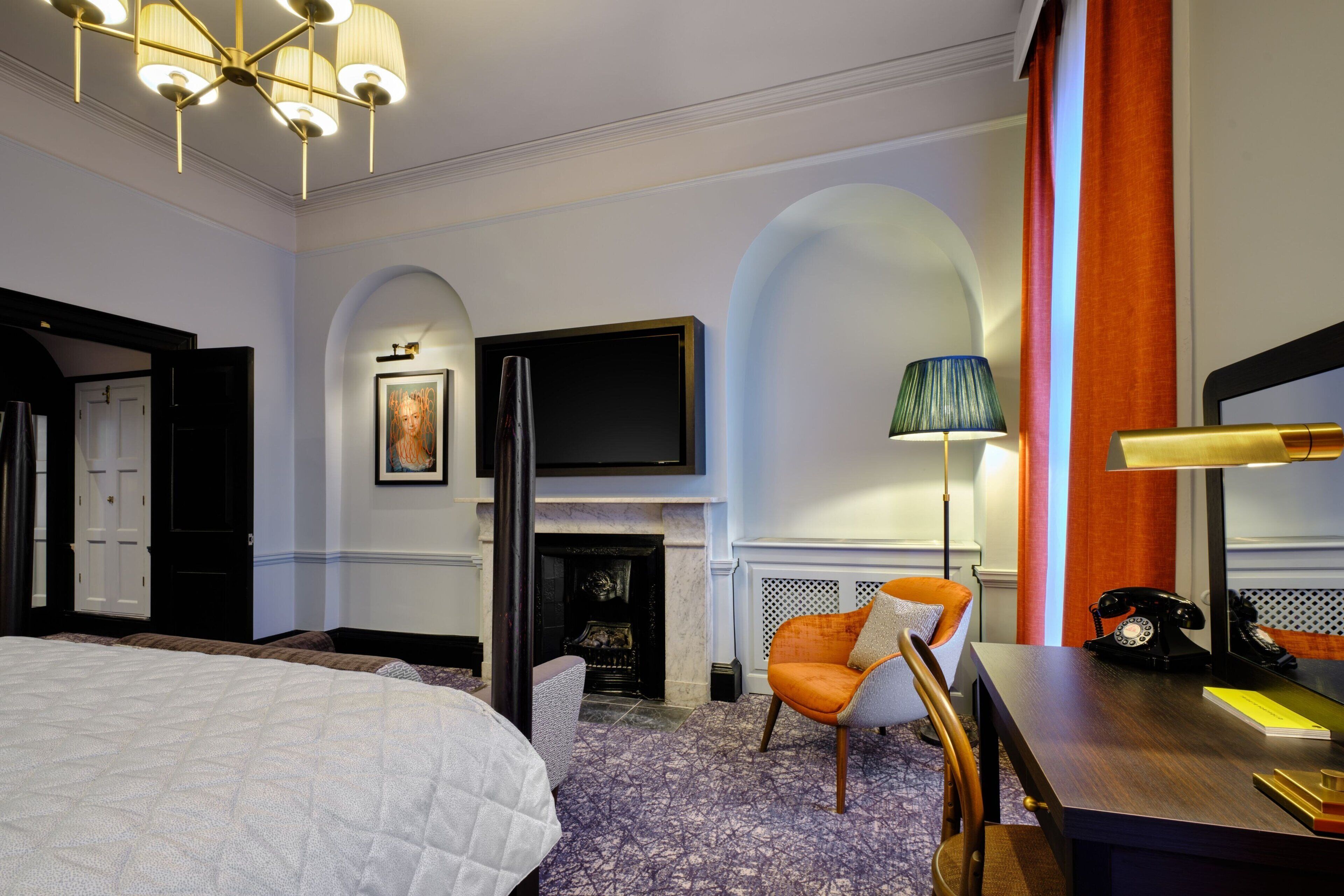 A hotel room with a large bed, a fireplace, a television, and a desk with a telephone.