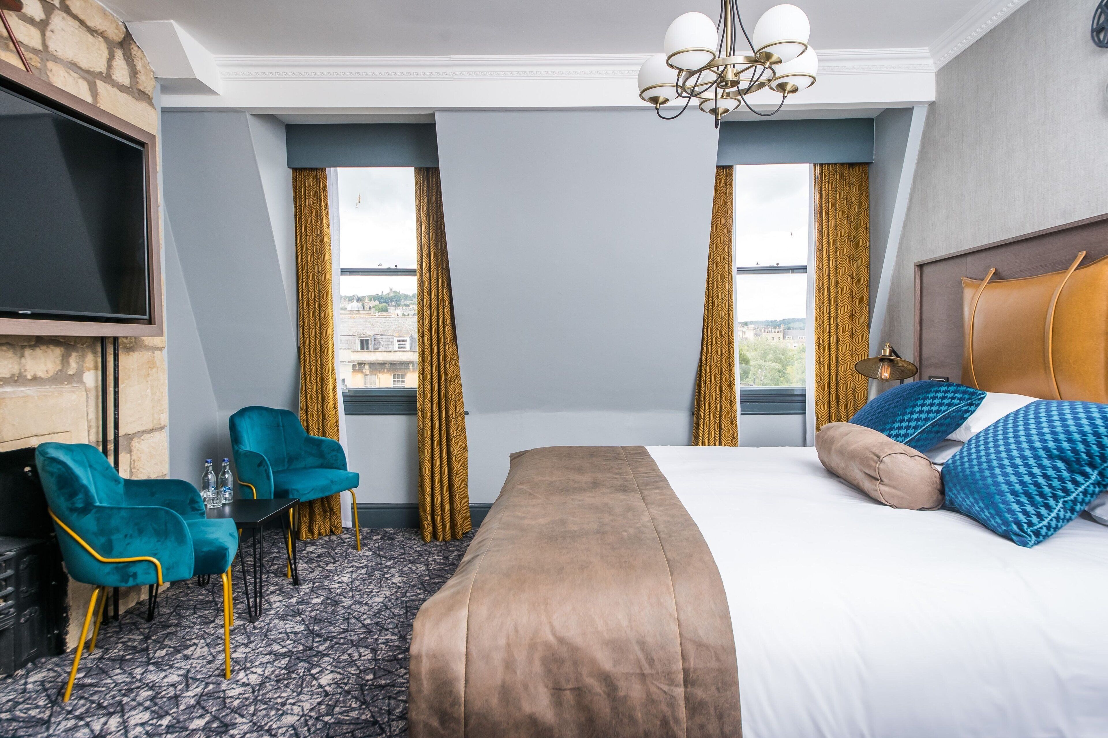 A hotel room with a bed, two chairs, a TV, and a view of the city.