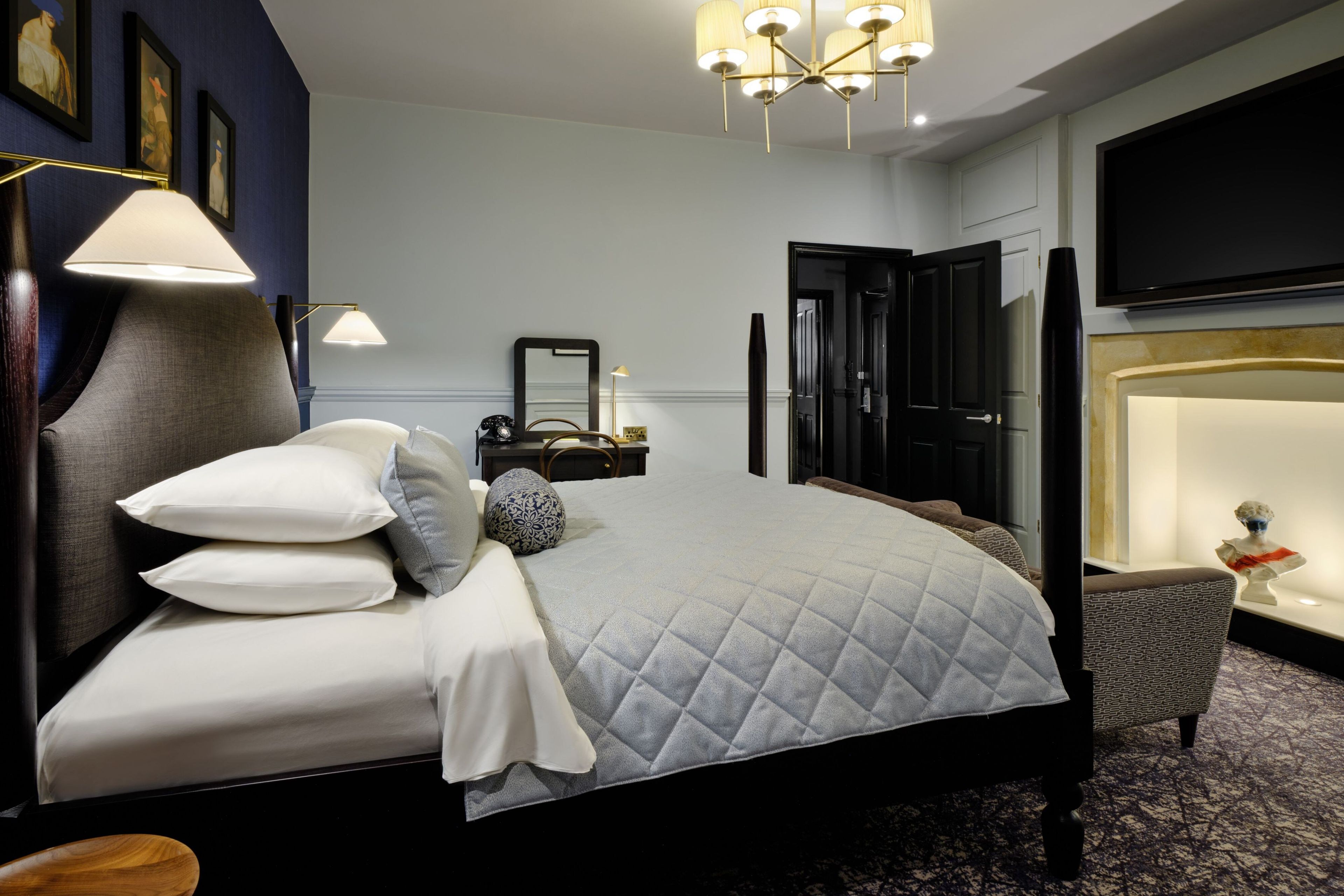 A hotel room with a bed, bedside lamps, a mirror, a telephone, a chair, and a television on the wall.