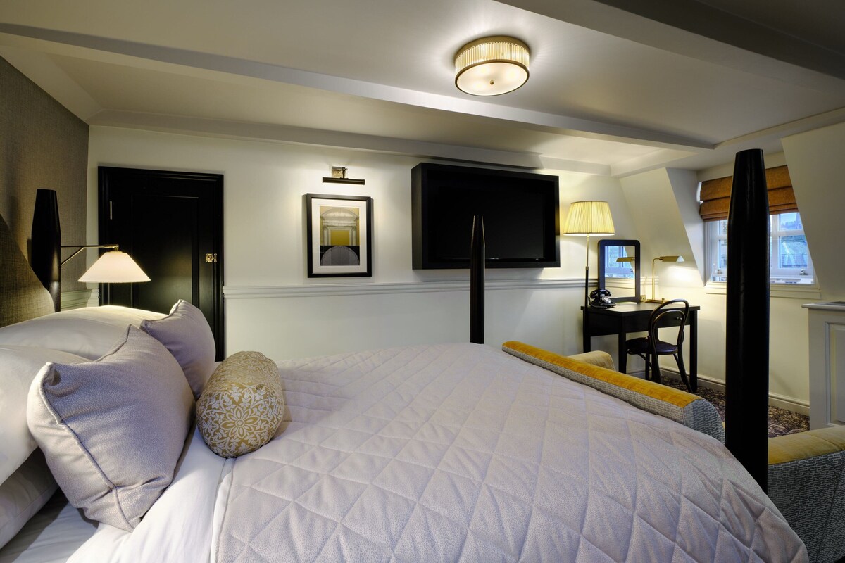 A hotel room with a large bed, a desk with a chair, a flat-screen TV, and a ceiling light fixture.