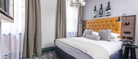 Ein Hotelzimmer mit einem großen Bett, einem Nachttisch mit Lampe, einer Kopfteil und einem an der Wand befestigten Telefon.