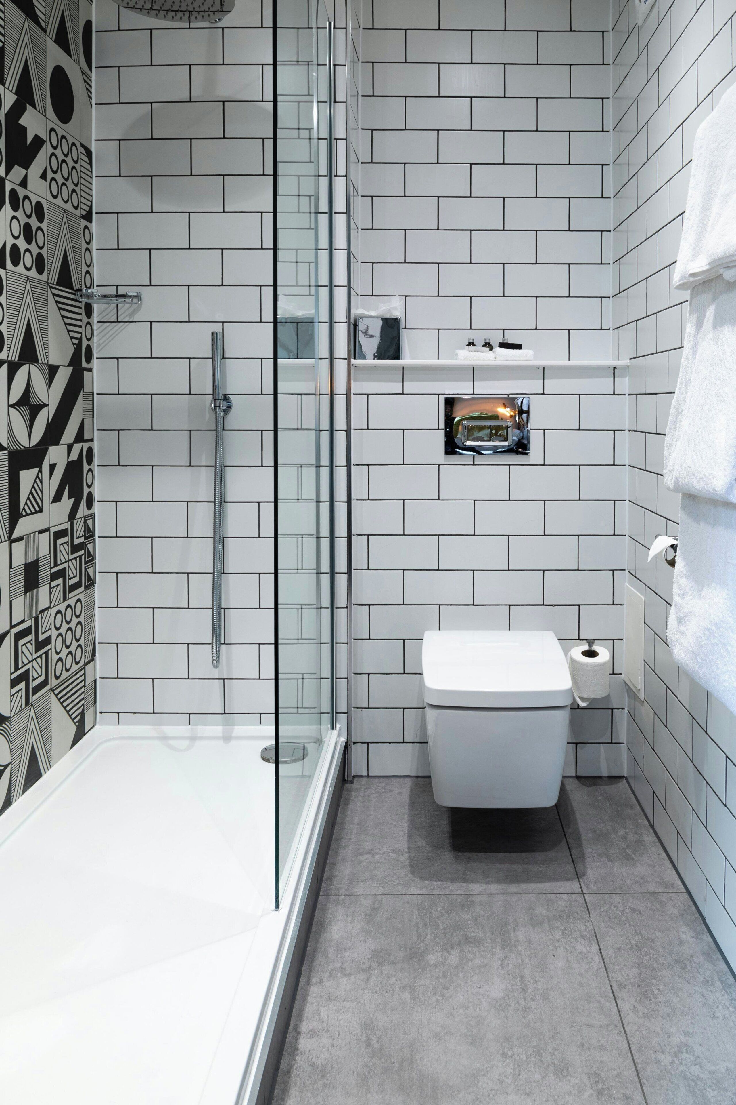 Ein modernes Badezimmer mit Duschkabine aus Glas, einer weißen Toilette und einem kleinen Ablagefach für Toilettenartikel.