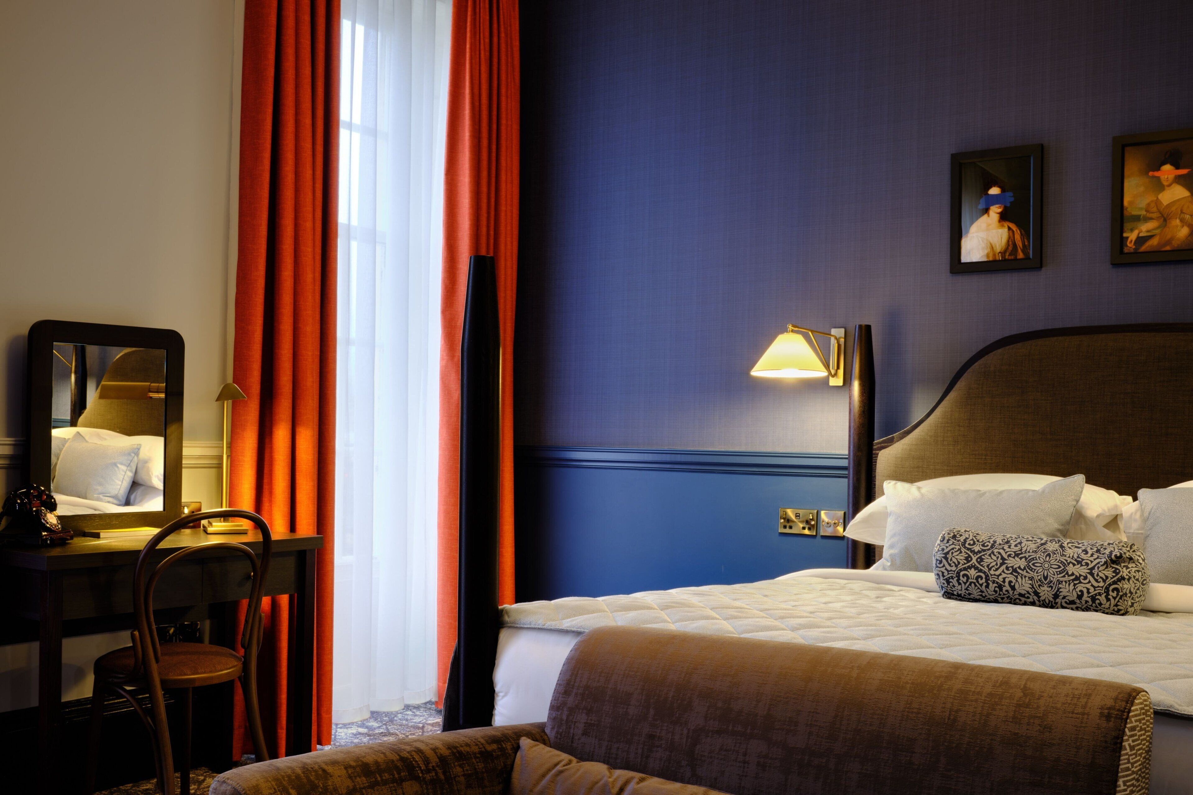 Et hotelværelse med en seng, et skrivebord, en stol og et natbord med en lampe.
