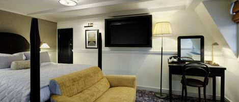 Habitación de hotel con cama, sofá, escritorio con silla, televisor de pantalla plana y lámpara.