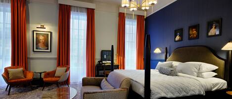 A hotel room with a large bed, two armchairs, a small table, and a chandelier.