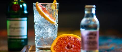 Ein Glas mit einem Eisgetränk, einer Orangenscheibe, einer halben Grapefruit und einer Flasche Alkohol auf einer Holzoberfläche.