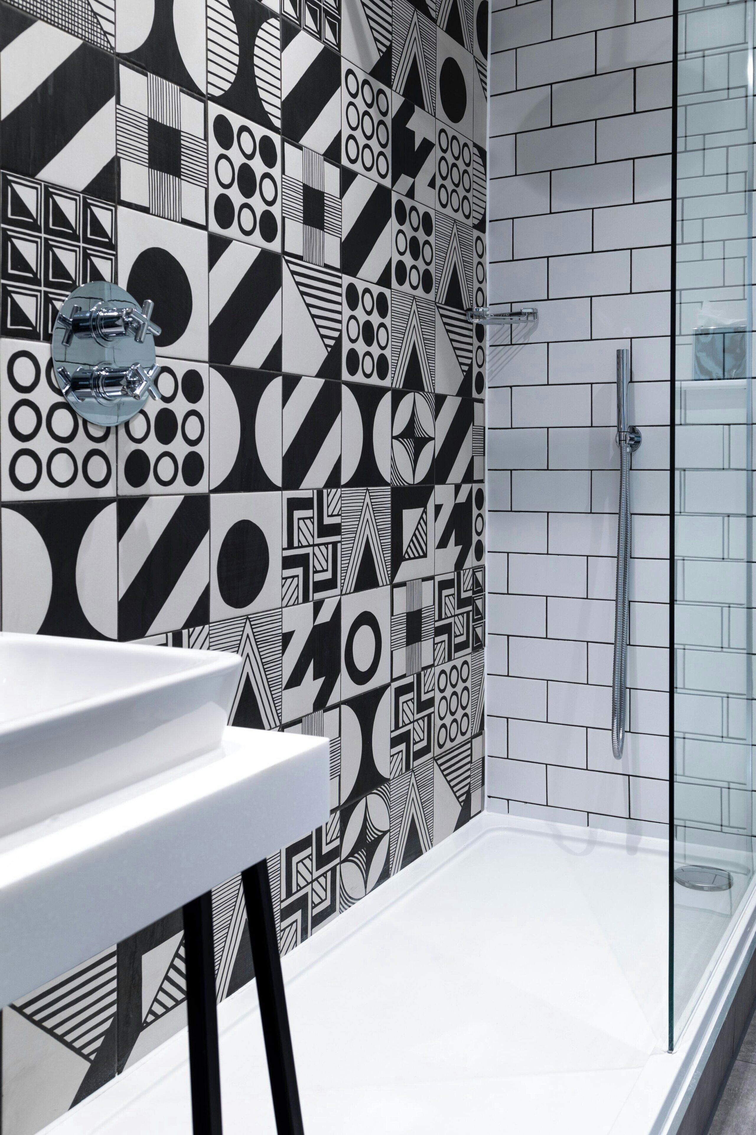 A bathroom with a geometric patterned wall, a white sink, and a glass shower enclosure.