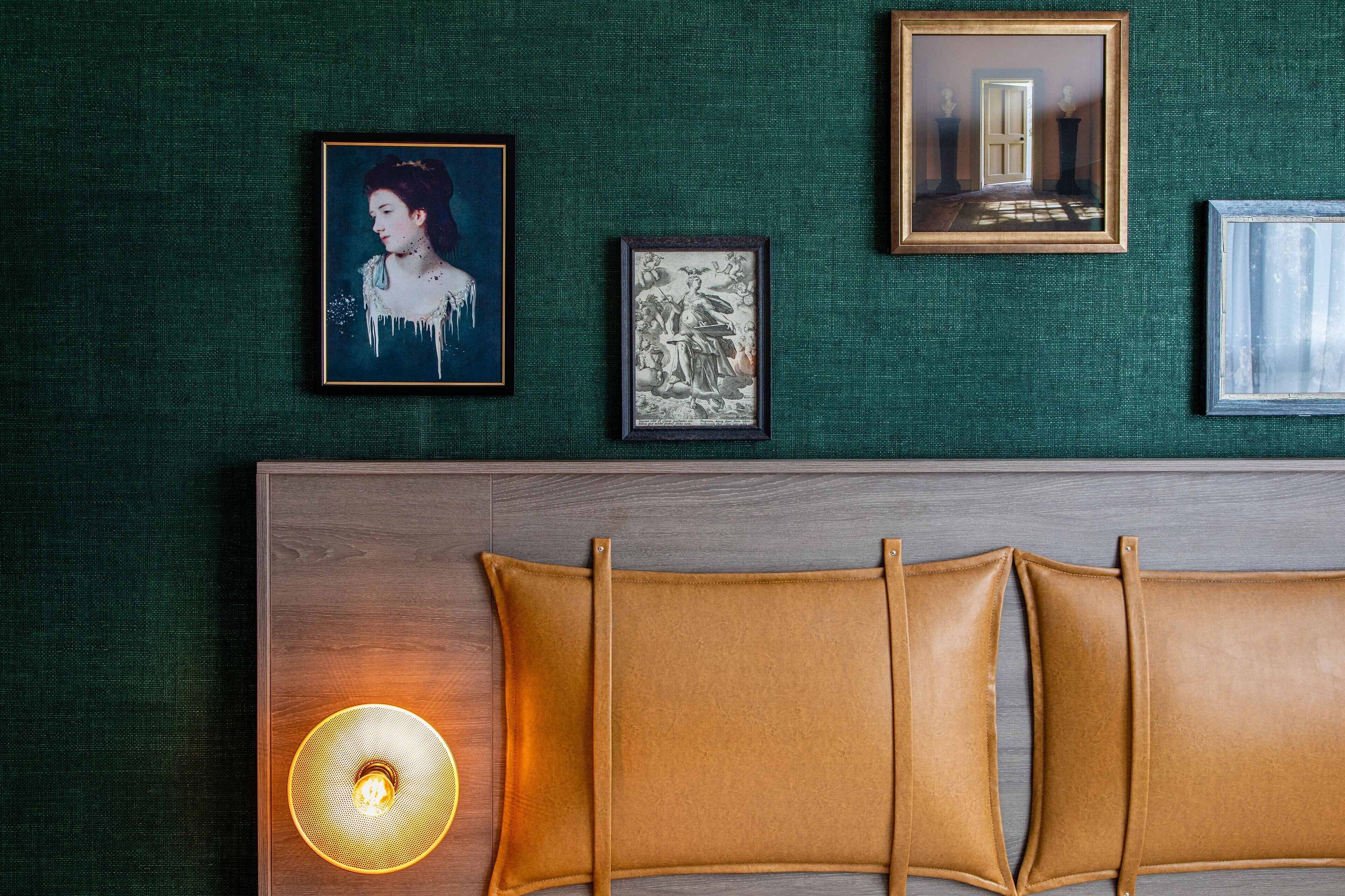 A room with a green textured wall, a wooden headboard with leather cushions, and three framed artworks.