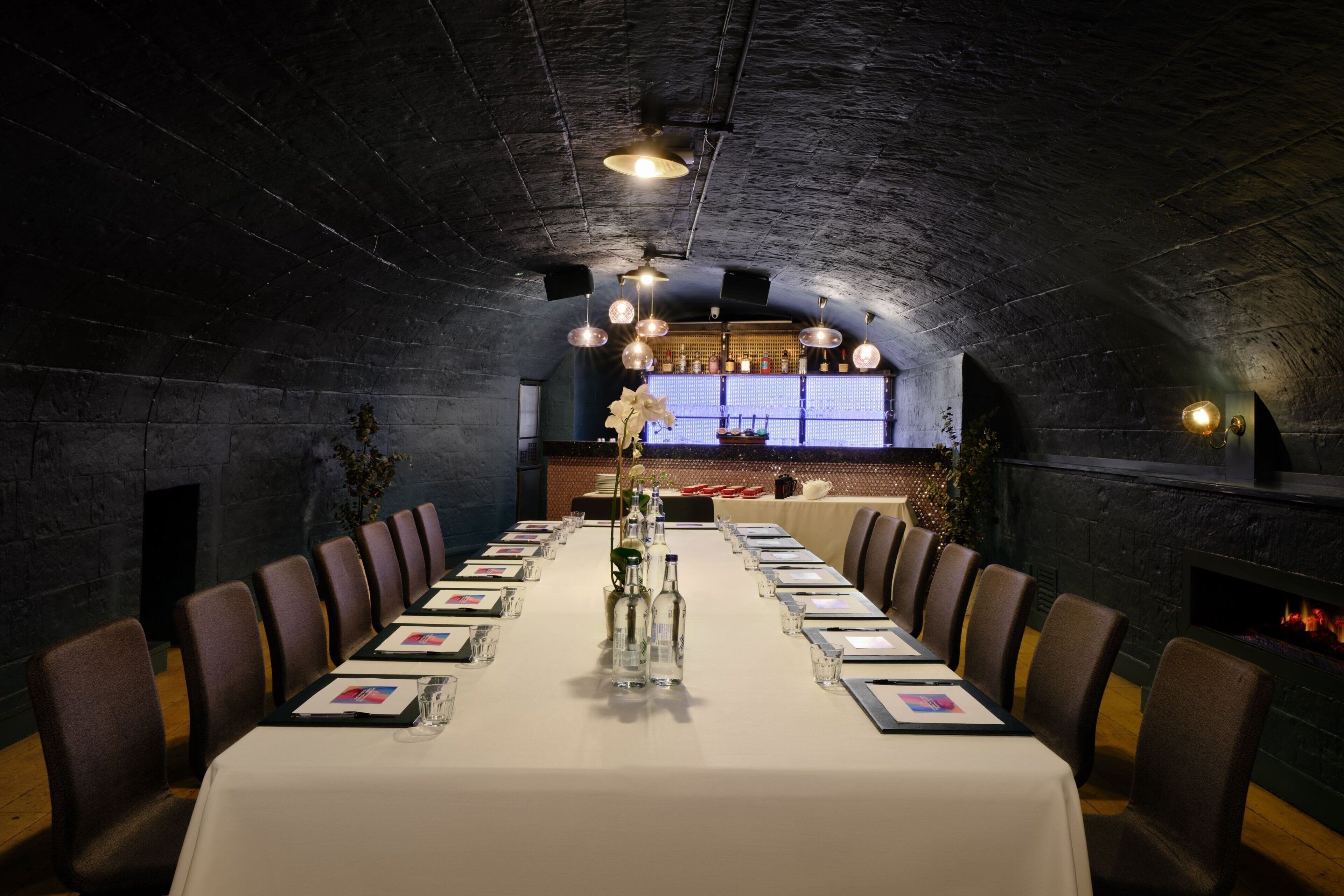A long dining table set for a meal in a room with a high, arched ceiling and stone walls.
