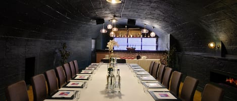 A long dining table set for a meal in a room with a high, arched ceiling and stone walls.