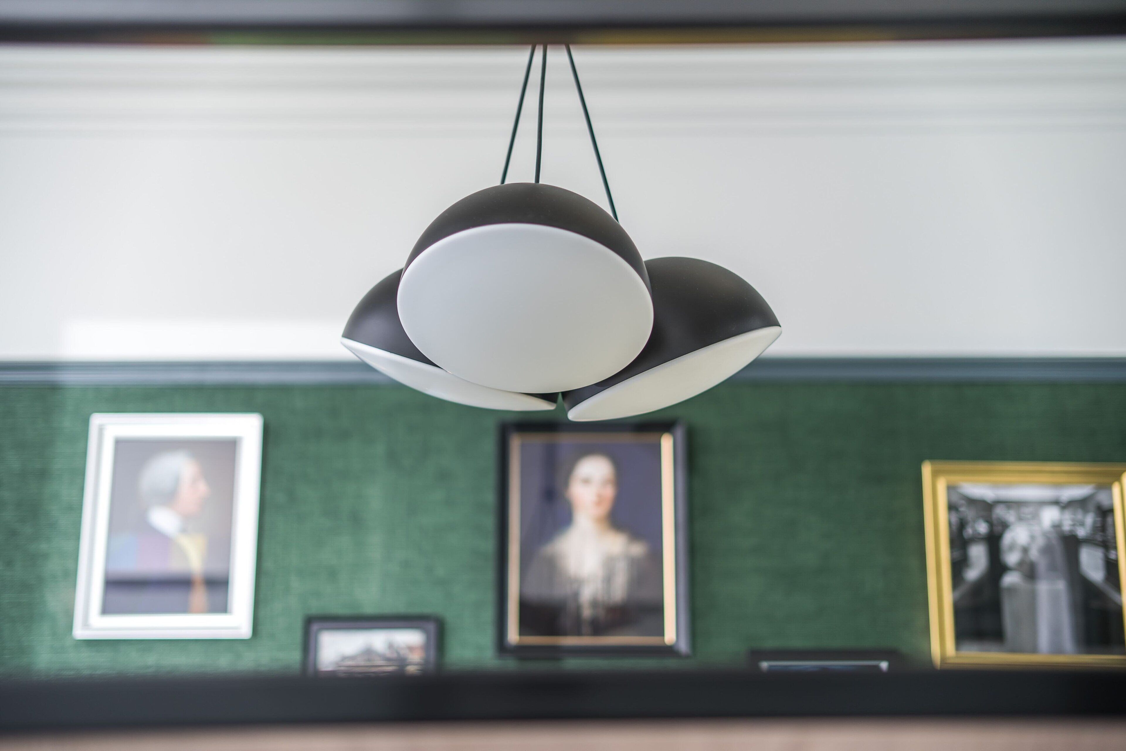 A modern chandelier with multiple arms and a central light source, hanging above a wall with framed pictures.