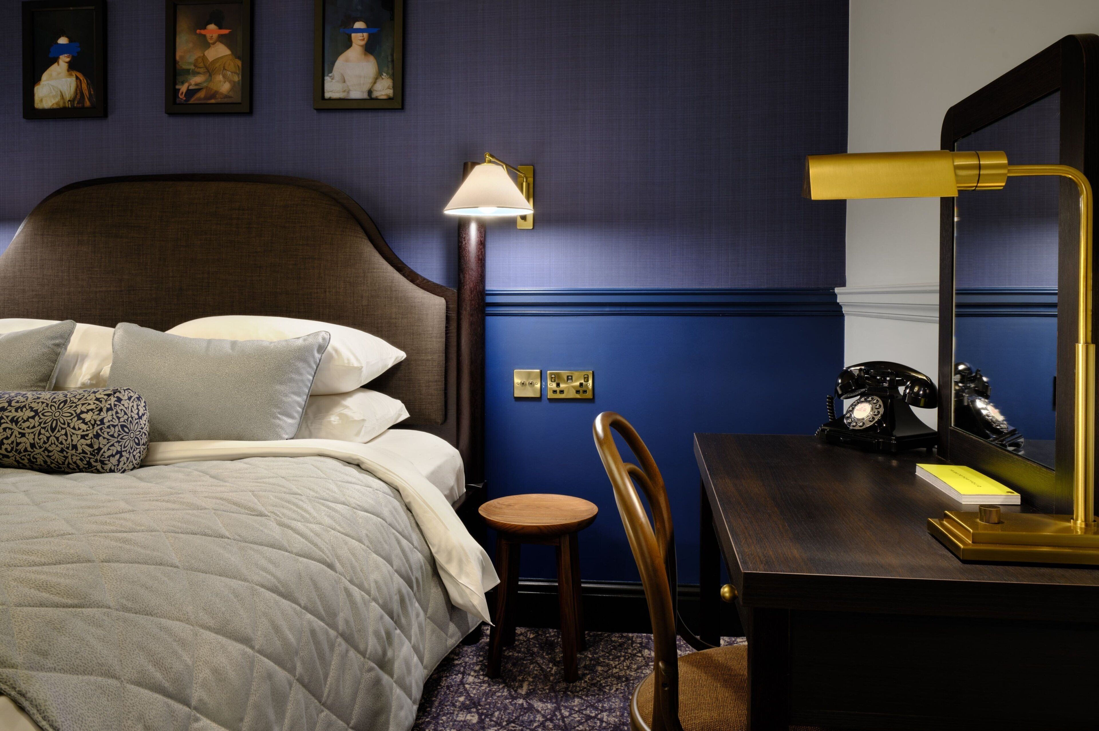 A hotel room with a bed, a desk with a lamp, a chair, and a telephone.