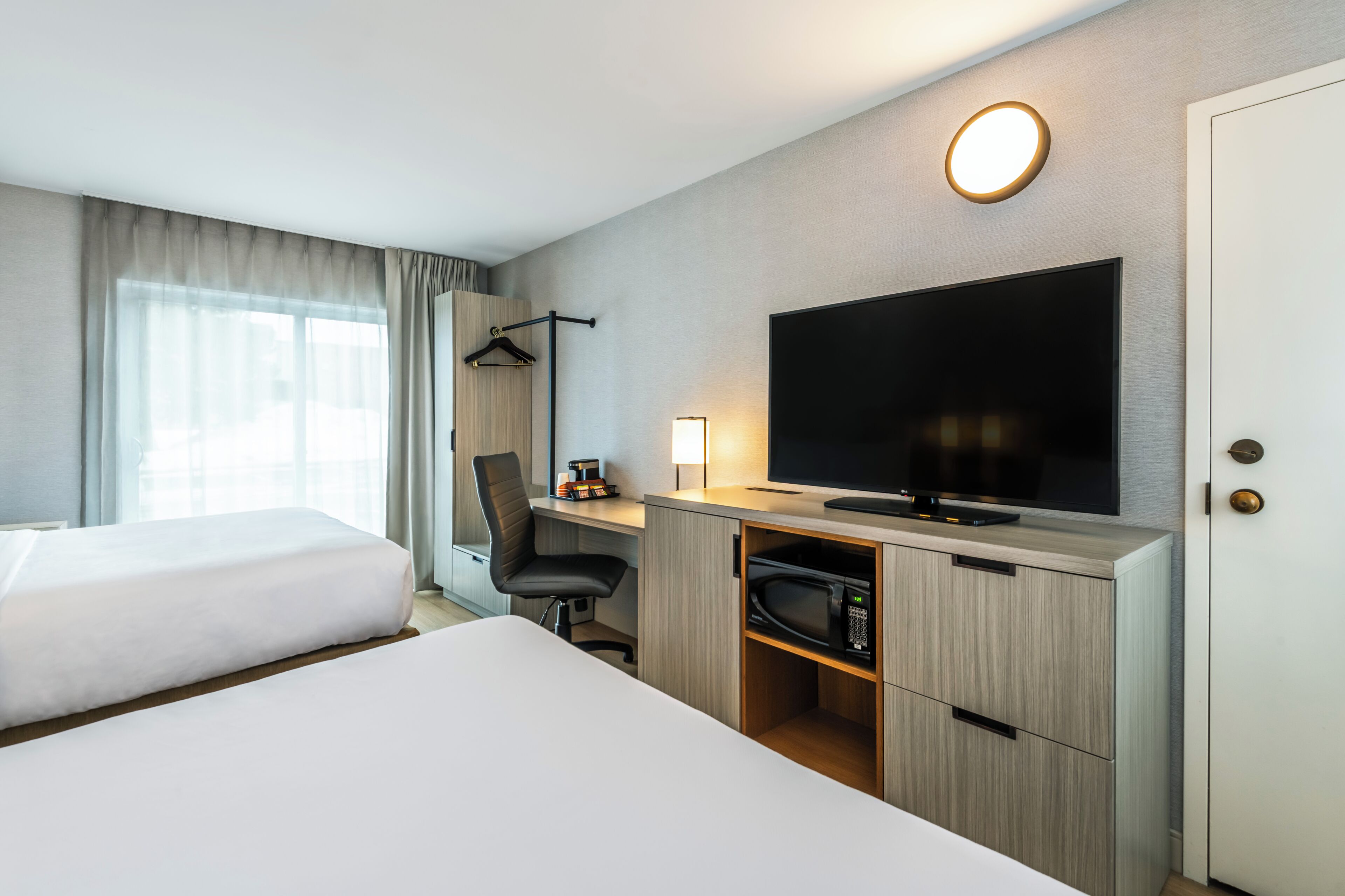 A hotel room with two beds, a desk with a flat-screen TV, a coffee maker, and a wardrobe.