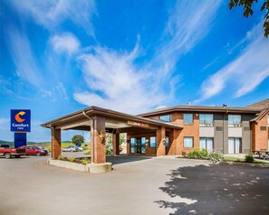 A Comfort Inn hotel with a covered parking area, a brick building, and a clear blue sky.