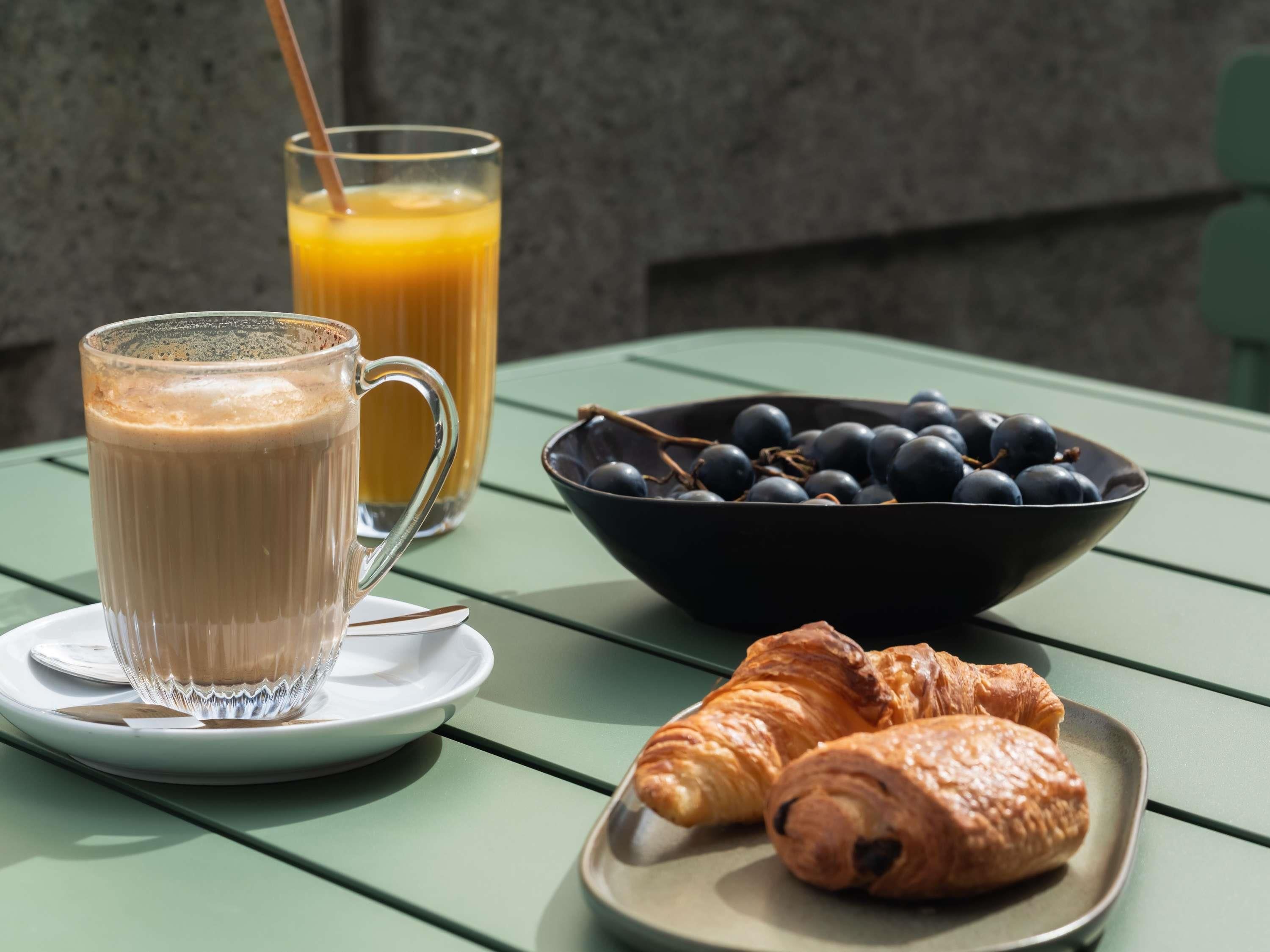 Ein Tisch mit einem Glas Orangensaft, einer Schüssel Blaubeeren und zwei Croissants.