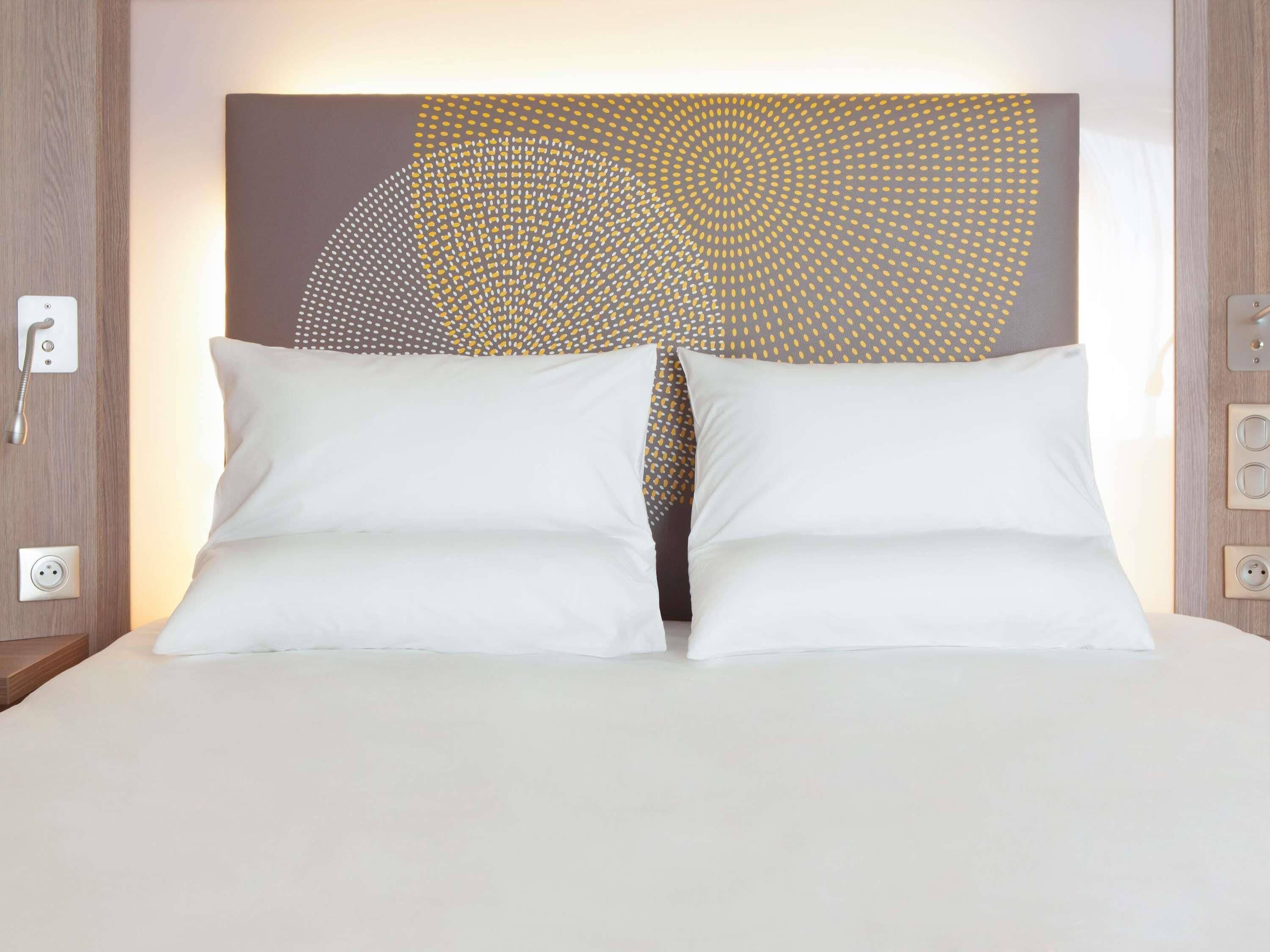 A bed with white pillows and a headboard with a geometric pattern.