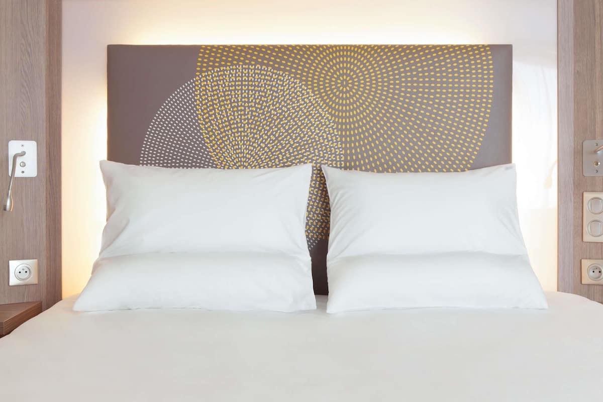 Una cama con almohadas blancas y un cabecero de diseño geométrico.