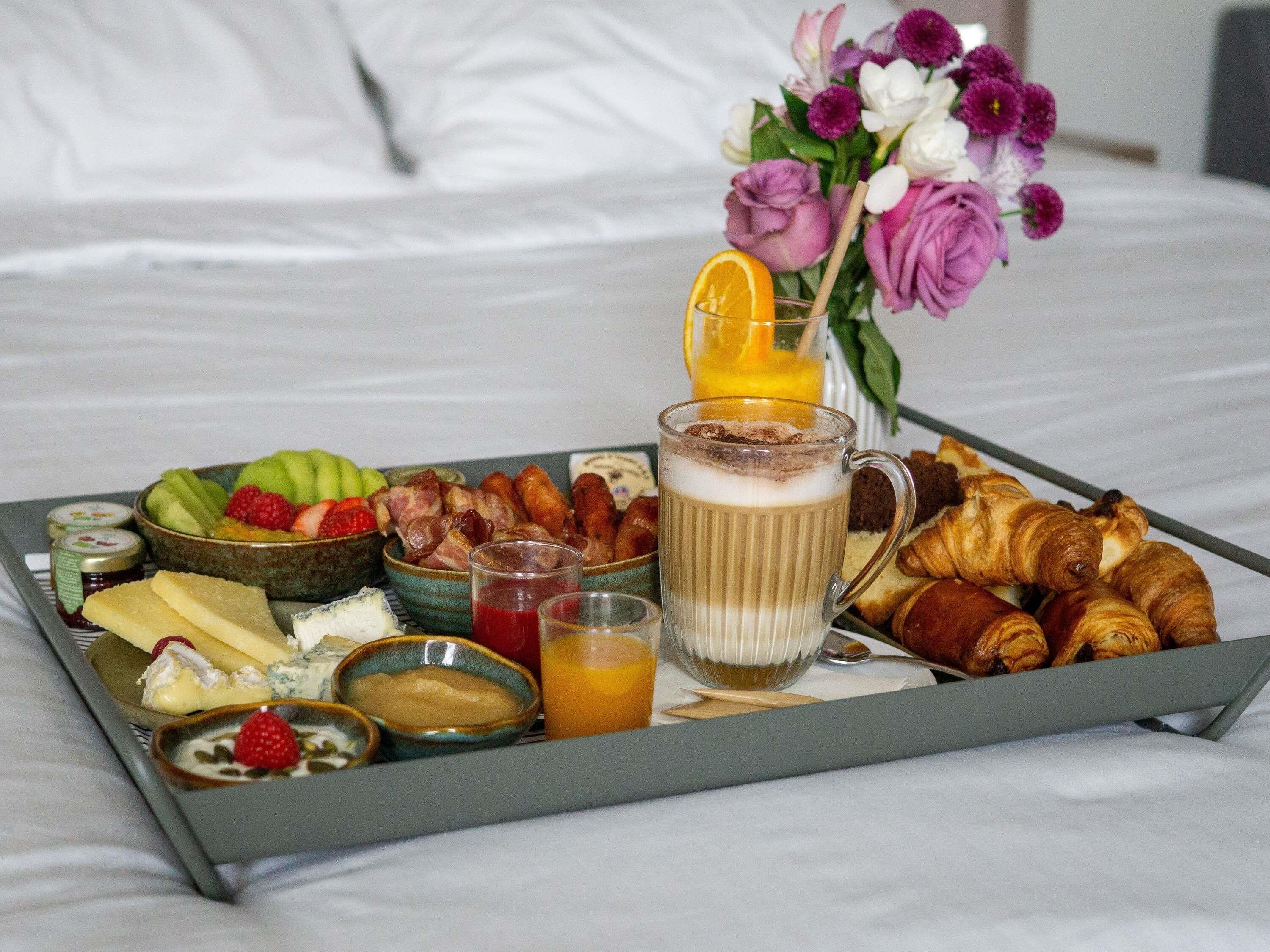 Ein Frühstücksbrett mit Croissants, Obst, Käse und einem Getränk auf einem Bett.