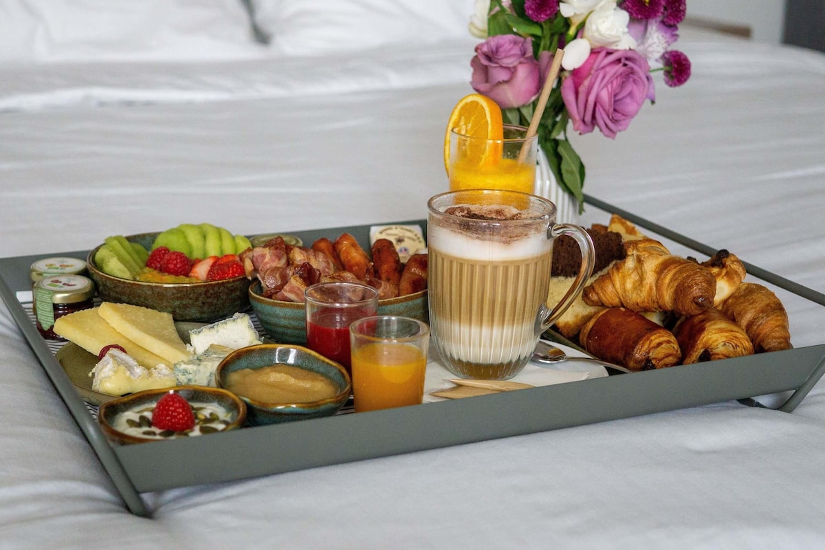 Un plateau de petit-déjeuner avec des croissants, des fruits, du fromage et une boisson, posé sur un lit.