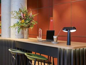 A modern reception desk with a laptop, a glass of iced coffee, a potted plant, and a lamp.