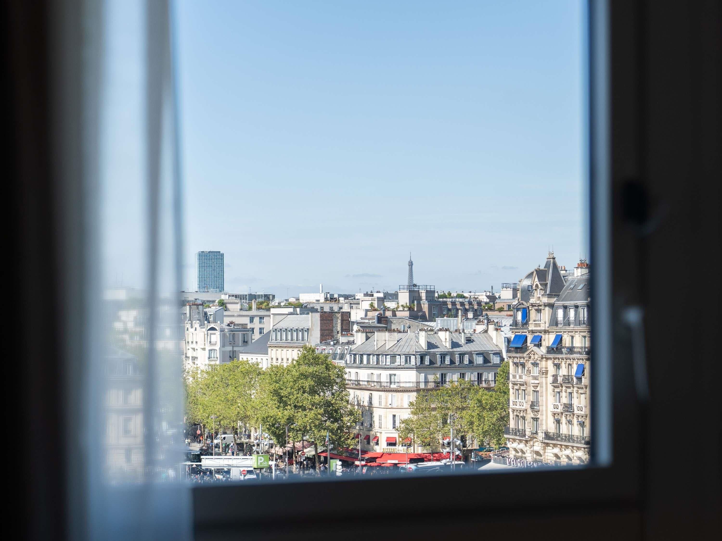 A cityscape through a window with buildings, a tower, and a clear sky.