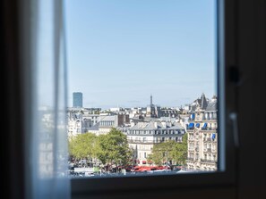 Un paisaje urbano a través de una ventana, con edificios, una torre y cielo despejado.