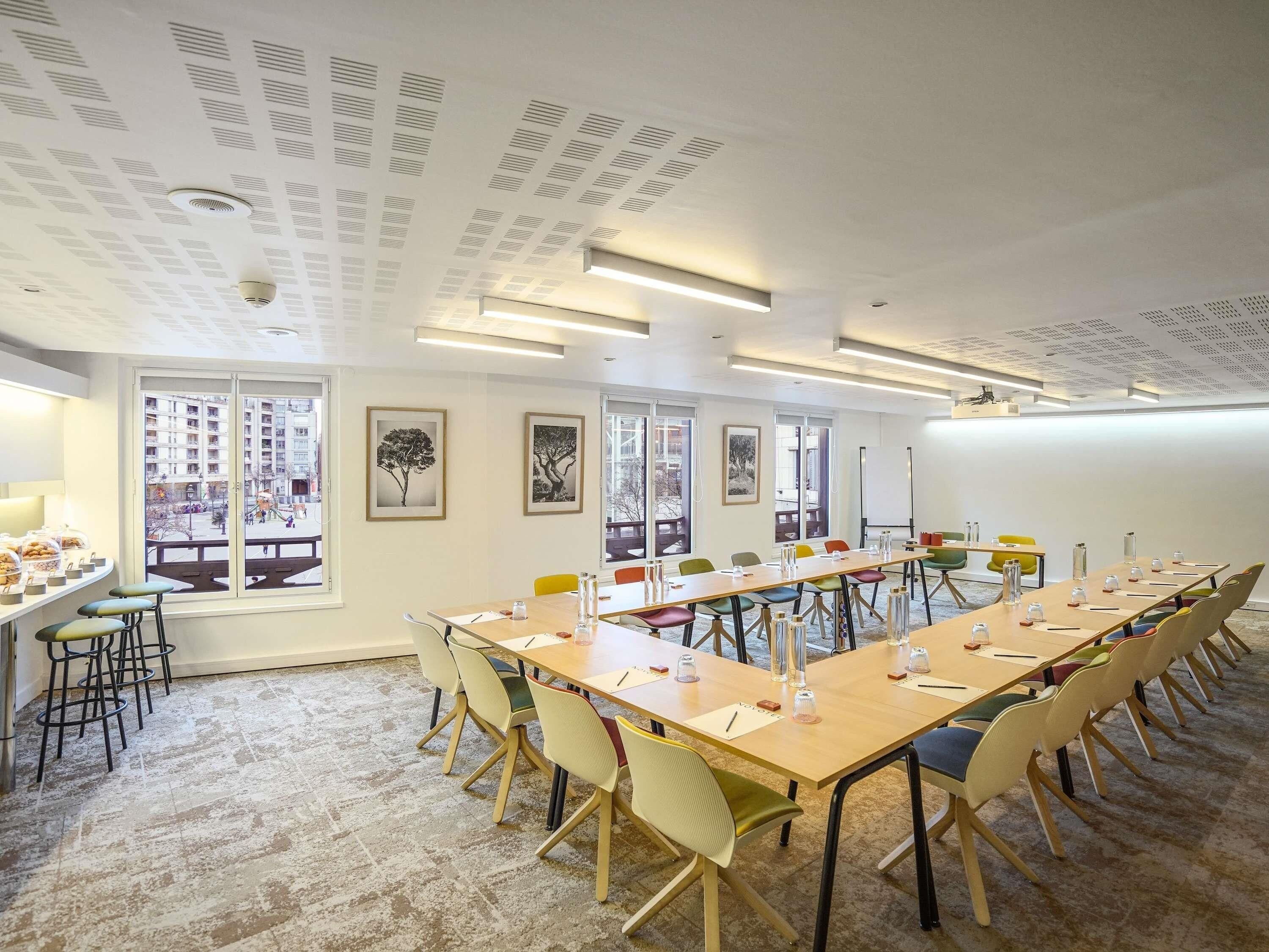 A conference room with a long table, chairs, and a view of buildings through large windows.