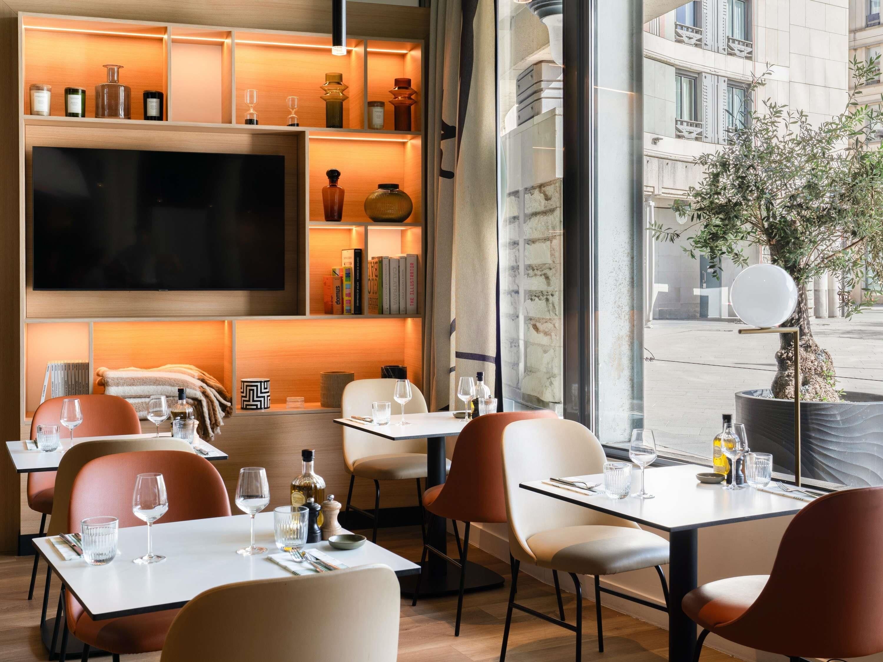 A modern dining area with tables, chairs, and a large flat-screen TV mounted on the wall.