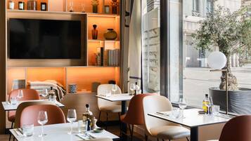A modern dining area with tables, chairs, and a large flat-screen TV mounted on the wall.