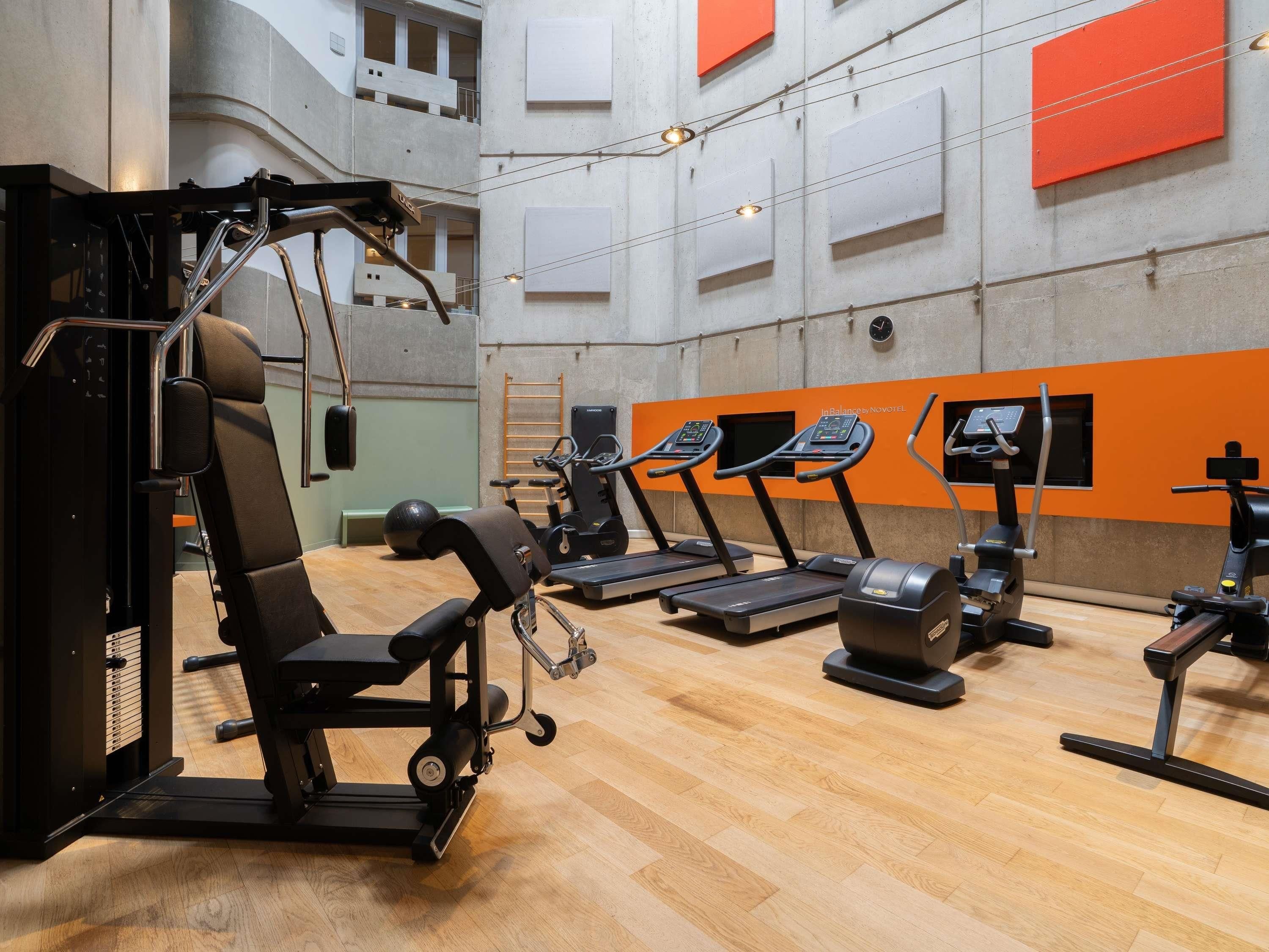 A gym with exercise equipment, a wooden floor, and orange accents on the walls.