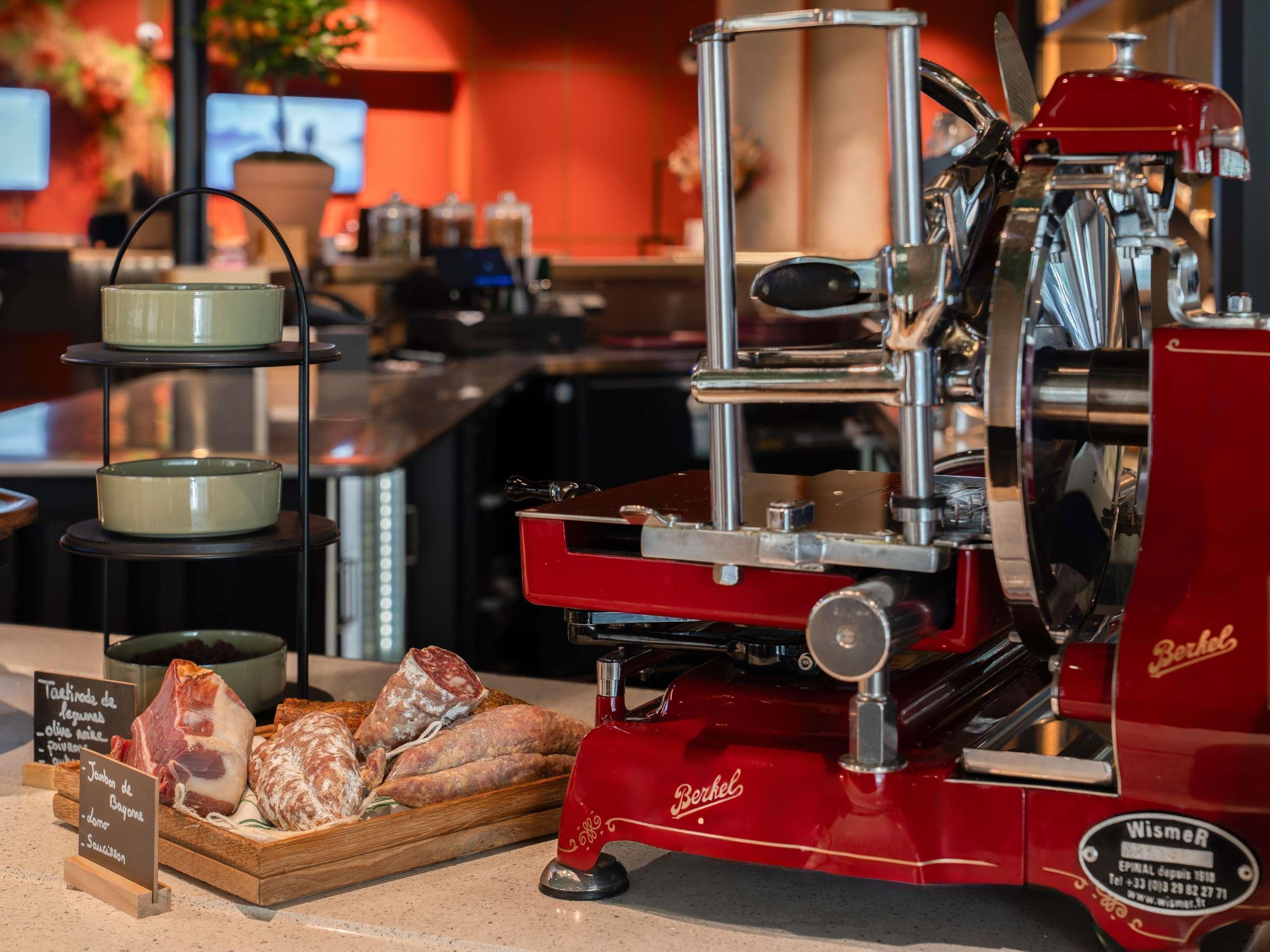 A coffee machine with a red exterior, a tray of cured meats, and a sign with food options.