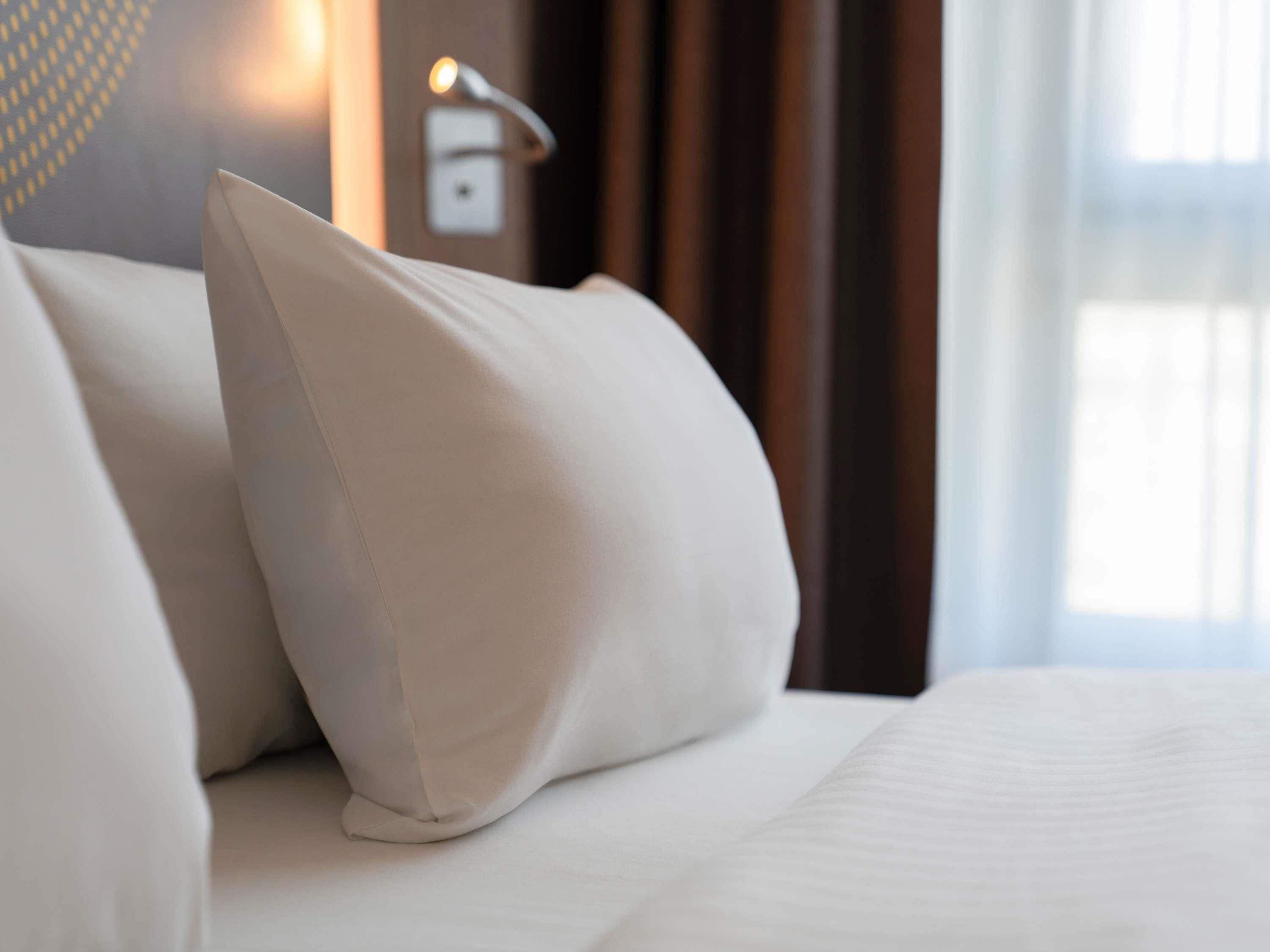 Een net opgemaakt bed met witte lakens en één kussen.