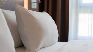 Een net opgemaakt bed met witte lakens en één kussen.