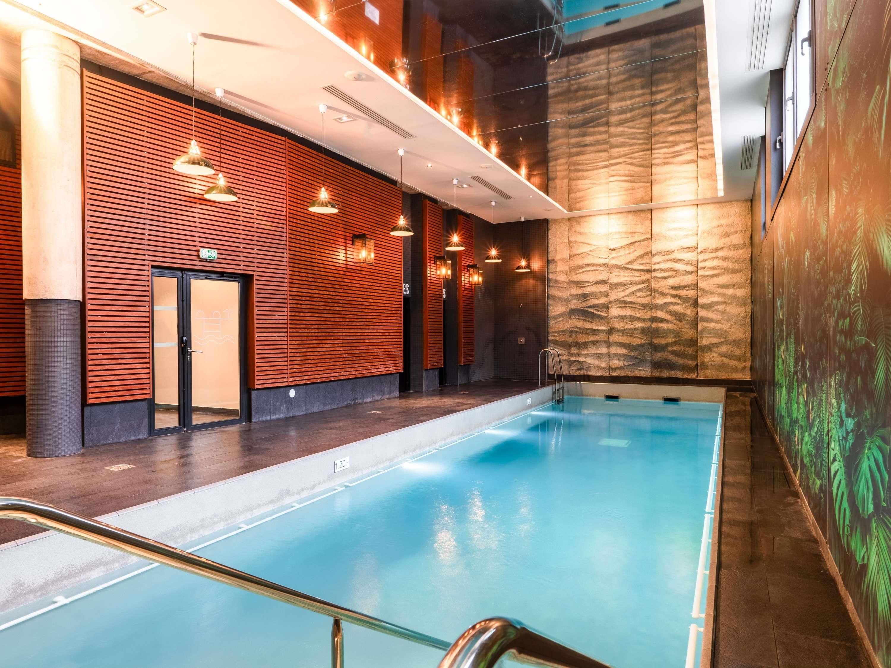 An indoor swimming pool with a modern design, featuring a long, narrow pool and a wooden wall with horizontal slats.
