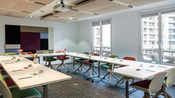 Sala de conferências com uma mesa comprida, cadeiras coloridas, um projetor e grandes janelas com vista para a cidade.