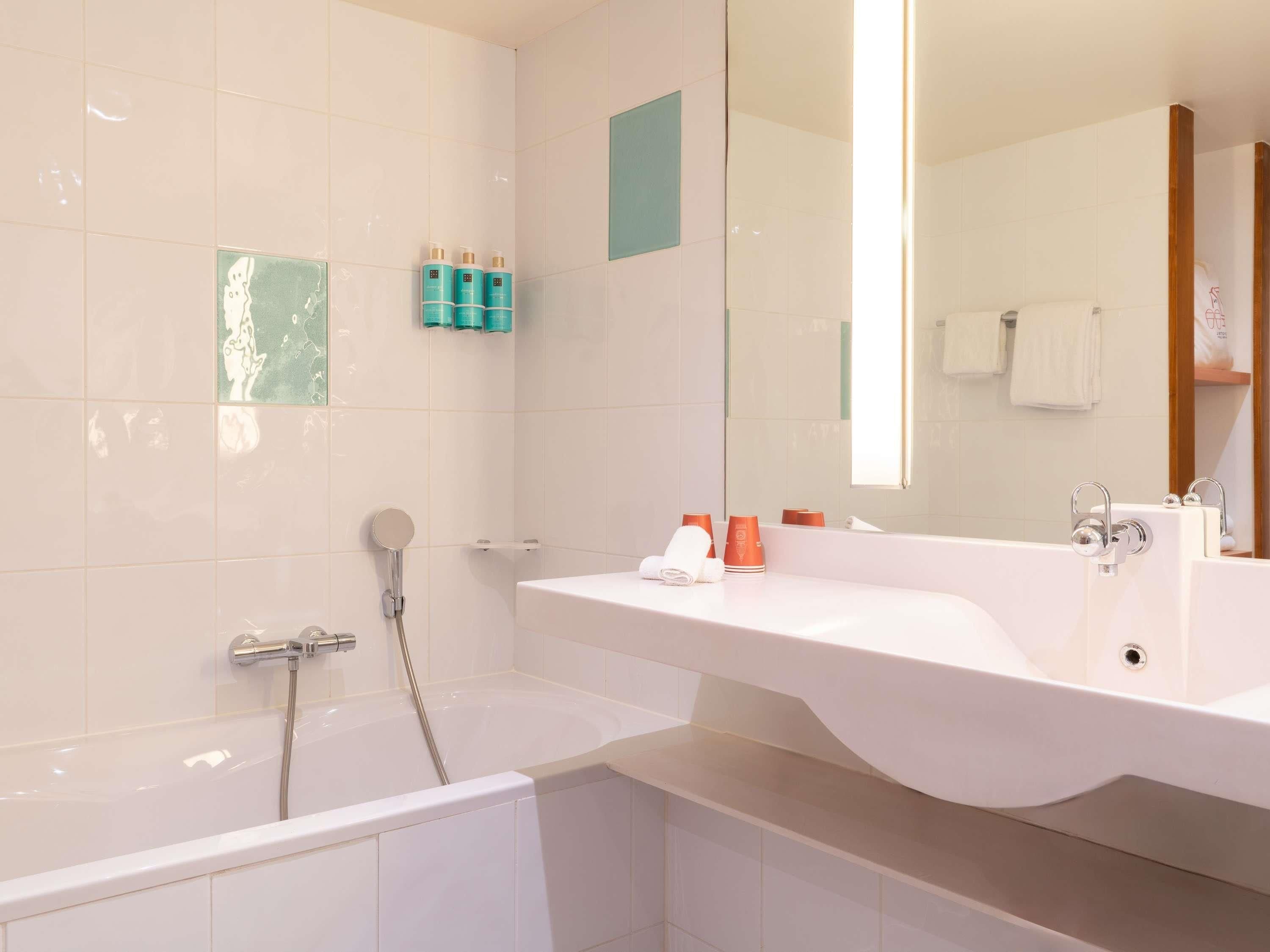 A modern bathroom with a bathtub, a large mirror, and a vanity with toiletries.