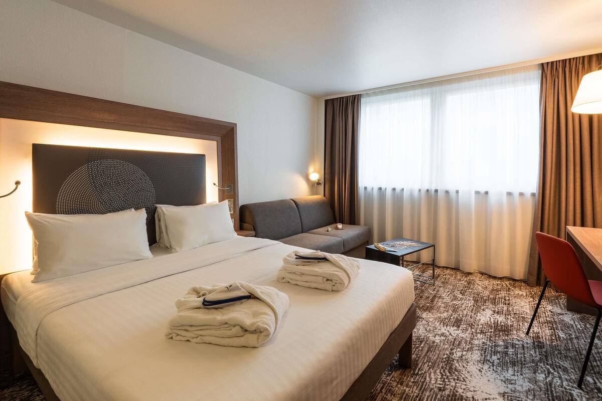 A hotel room with a large bed, a sofa, a small table, and a desk.