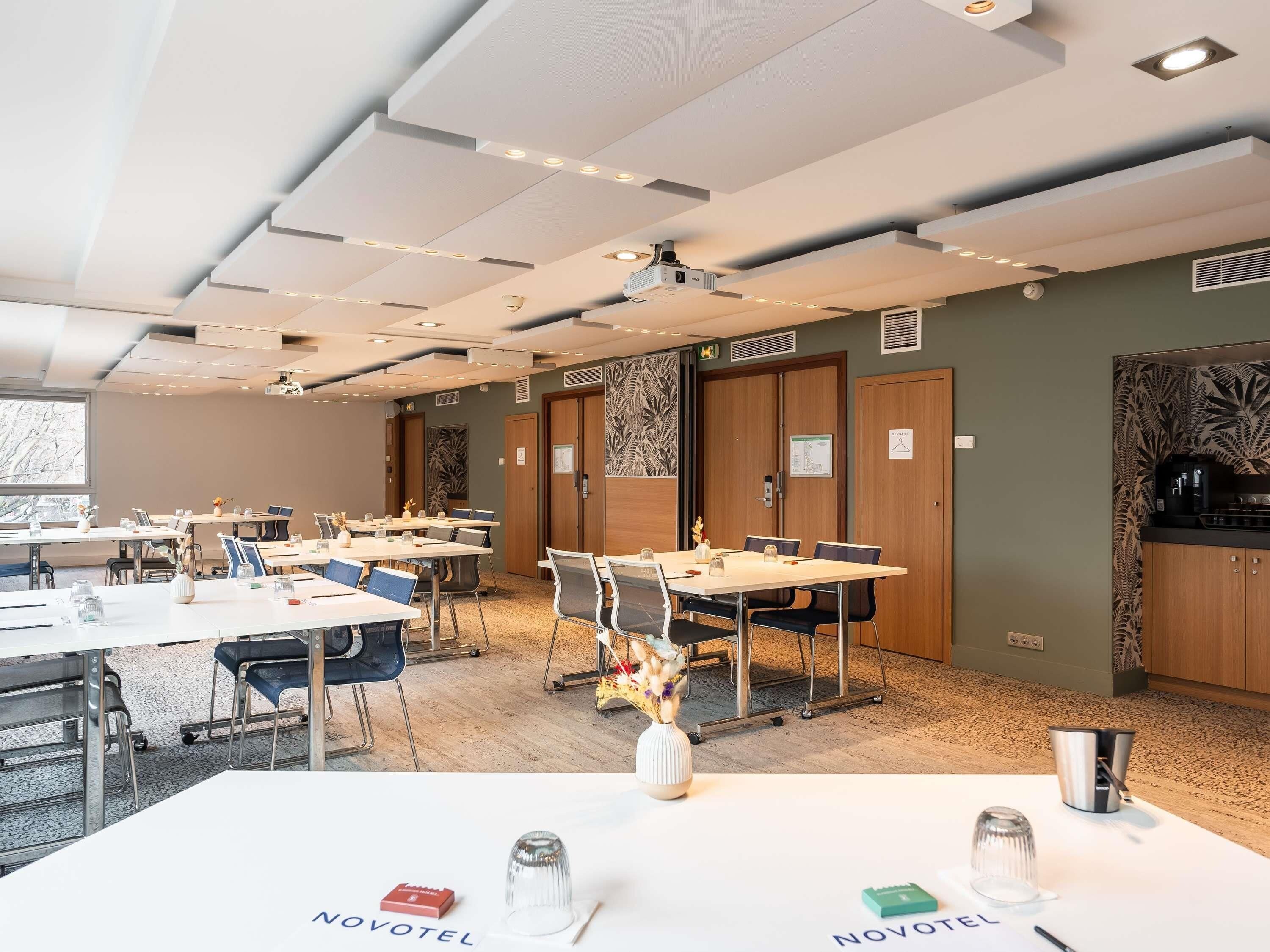 A hotel room with a conference table, chairs, a projector, and a kitchenette.