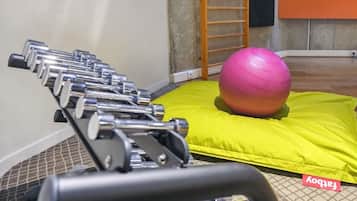 A gym with exercise equipment and a pink exercise ball on a yellow mat.