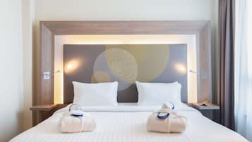 Ein Hotelzimmer mit einem großen Bett, zwei Nachttischen, einer Wandleuchte und einem Fenster mit Vorhängen.