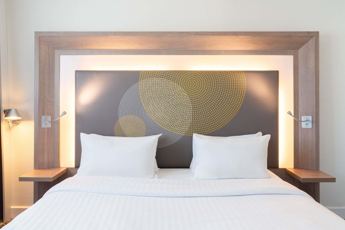 A hotel room with a large bed, two bedside tables, and a wall art piece.