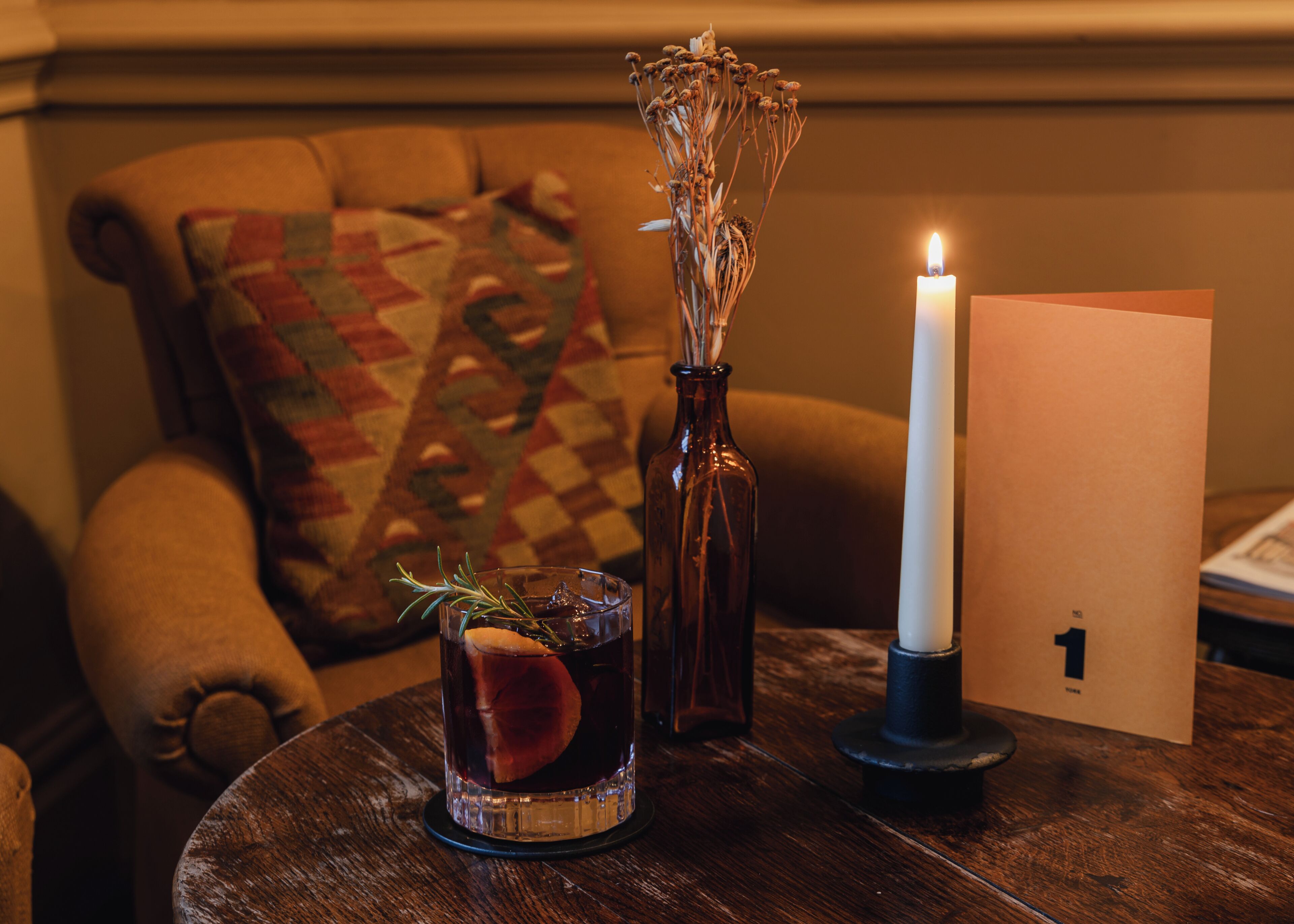 A wooden table with a glass of iced tea, a candle, and a card.