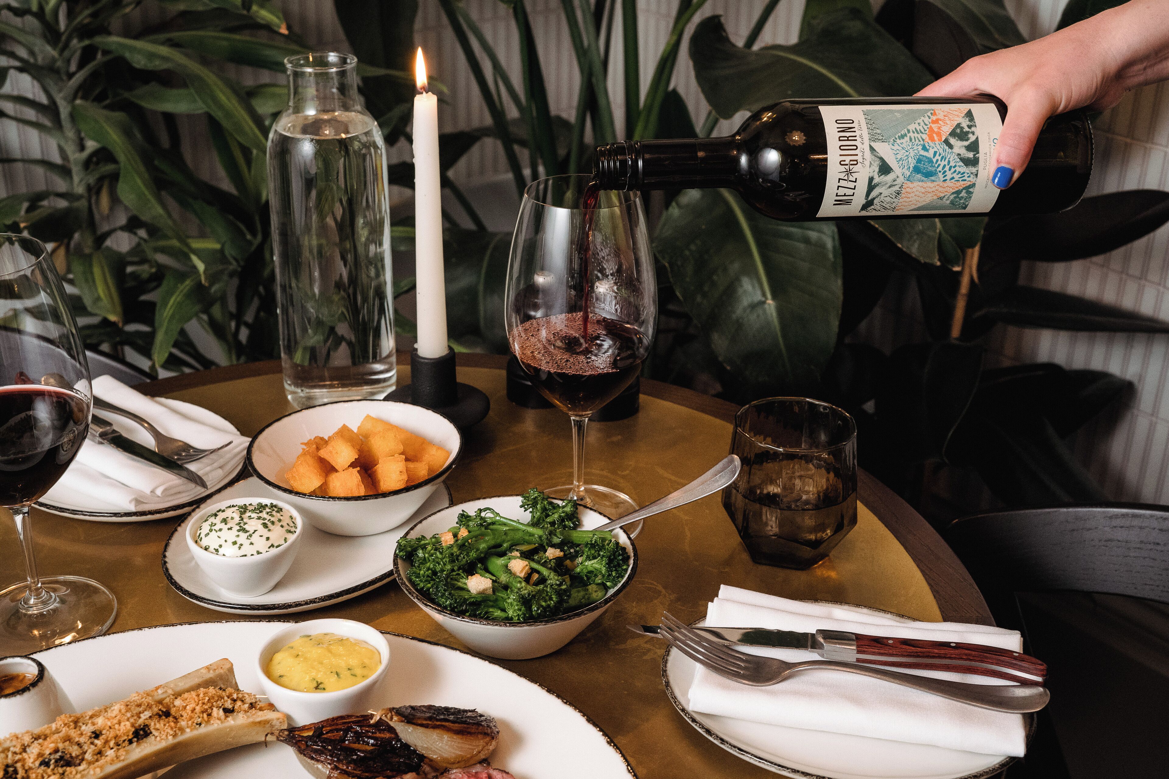 A table set with a candle, a bottle of wine, a glass of wine, a bowl of salad, and various side dishes.